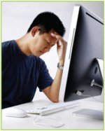 Man sitting at his computer with his head in his hands suffering from a headache due to poor ergonomic awareness.