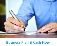 Image of man in blue shirt, showing just his left, and right hand with pen writing down ideas for his business plan..