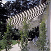 Striped domestic awning fitted to side of house overlooking garden.
