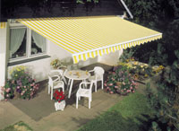 Striped yellow and white garden awning or canopy, protecting patio table and chairs from the sun.